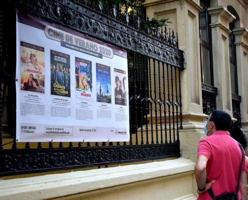 Una pareja observa, desde la acera, la cartelera con as películas del Cine de Verano 2020 colocada en la verja del Chalet Fontecha