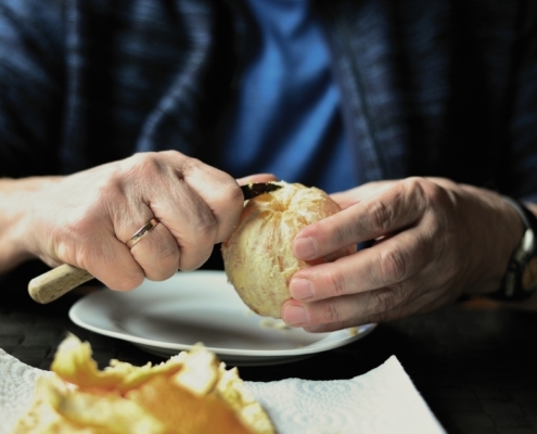 Detalle manos de una persona mayor pelando una naranja