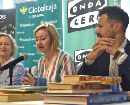 Primer plano libros con el diputado de Cultura, la presidenta de Asprona y la directora de Atresmedia Radio Albacete de fondo en desenfoque